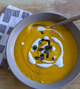 Bowl of pumpkin soup topped with coconut yoghurt drizzle and pumpkin seeds