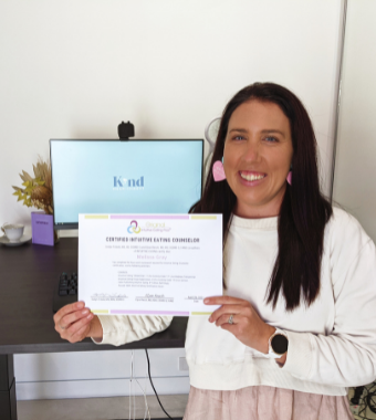 Woman holding certificate standing in front of computer and desk